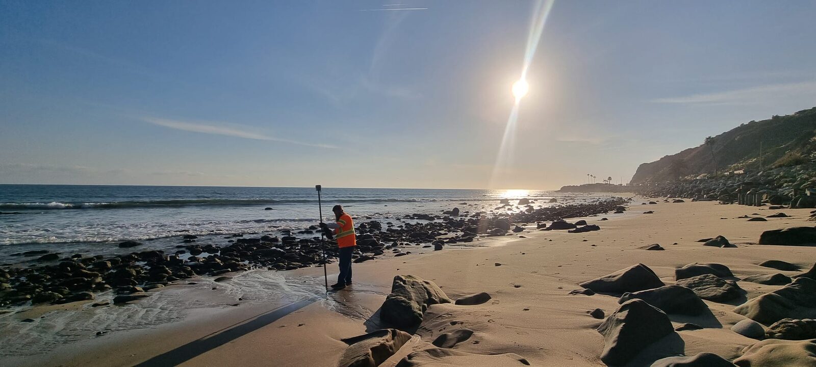 OCEAAN field team member surveying a rocky beach at sunset